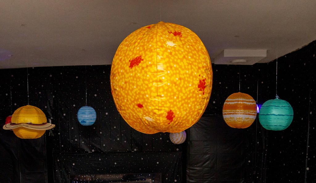 Hanging inflatable planets in a black starry room, part of a Toy Story Pizza Planet birthday party setup.