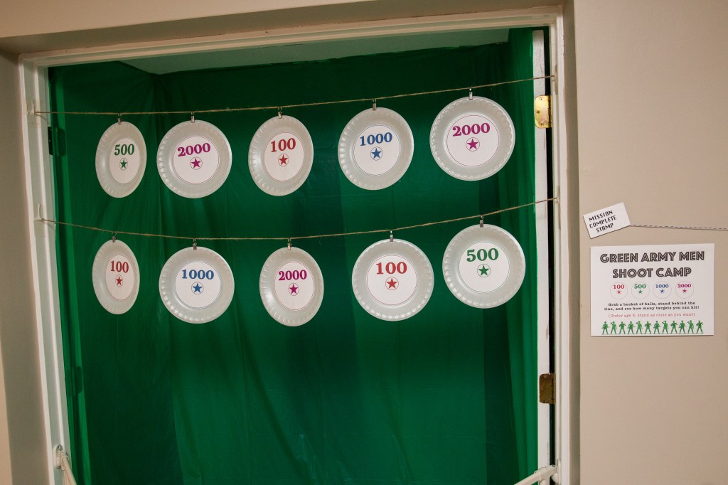 Toy Story-themed target game with paper plates labeled with point values like 500 and 2000, strung in front of a green backdrop as kids throw balls to score.