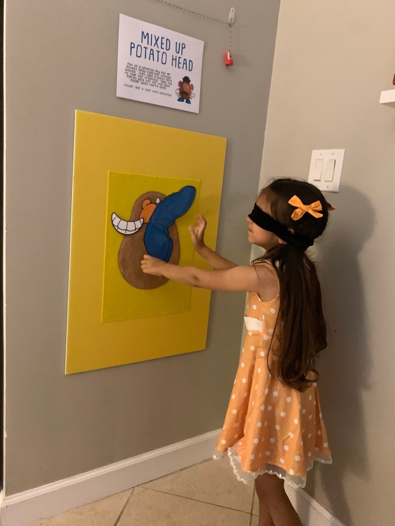 A blindfolded child attempts to stick a felt body part onto a large Mr. Potato Head poster as part of a birthday party game inspired by Toy Story.