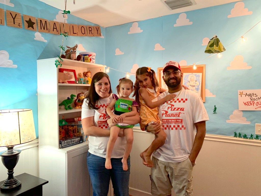 Family photo in front of Andy’s Room backdrop with Toy Story toys and Pizza Planet shirts