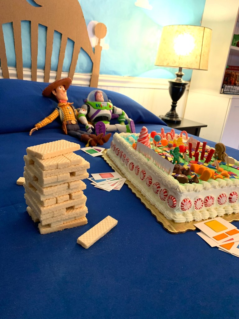 Toy Story birthday scene with Candyland cake, Woody and Buzz dolls, and a Jenga tower made of wafer cookies