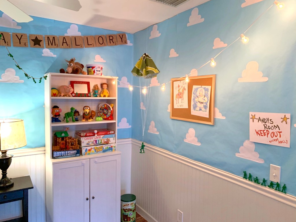 Toy Story-themed bedroom wall with custom cloud wallpaper, Toy Story toys on a shelf, and string lights