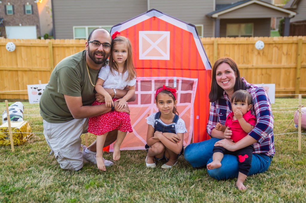 Laura with her husband and three children posing in front of a red barn backdrop at a farm-themed backyard birthday party.