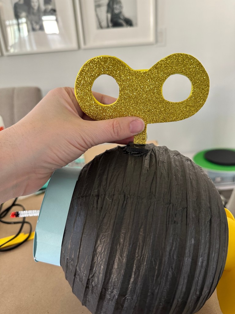 Hand holding glittery gold winder attached to the back of the Bob-omb lantern with hot glue.