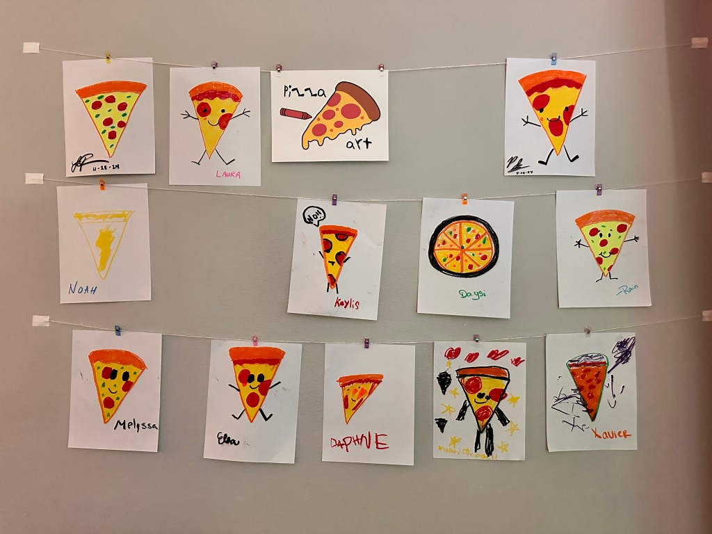 Pizza-themed drawings displayed on a wall with small clips during the Bubba’s Pizzeria party.