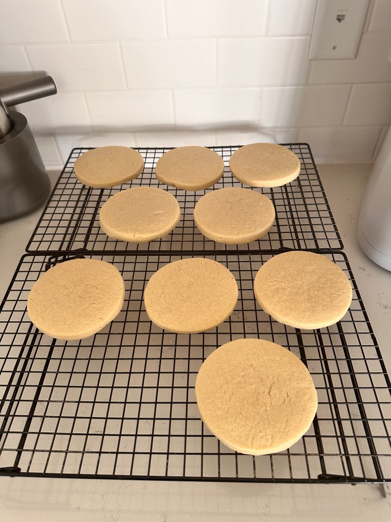 Nine round sugar cookies cooling on a black wire rack against a white tiled kitchen backsplash.