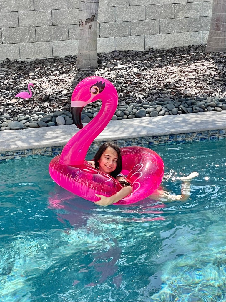 Close-up of a smiling girl relaxing on a large flamingo float in the pool
