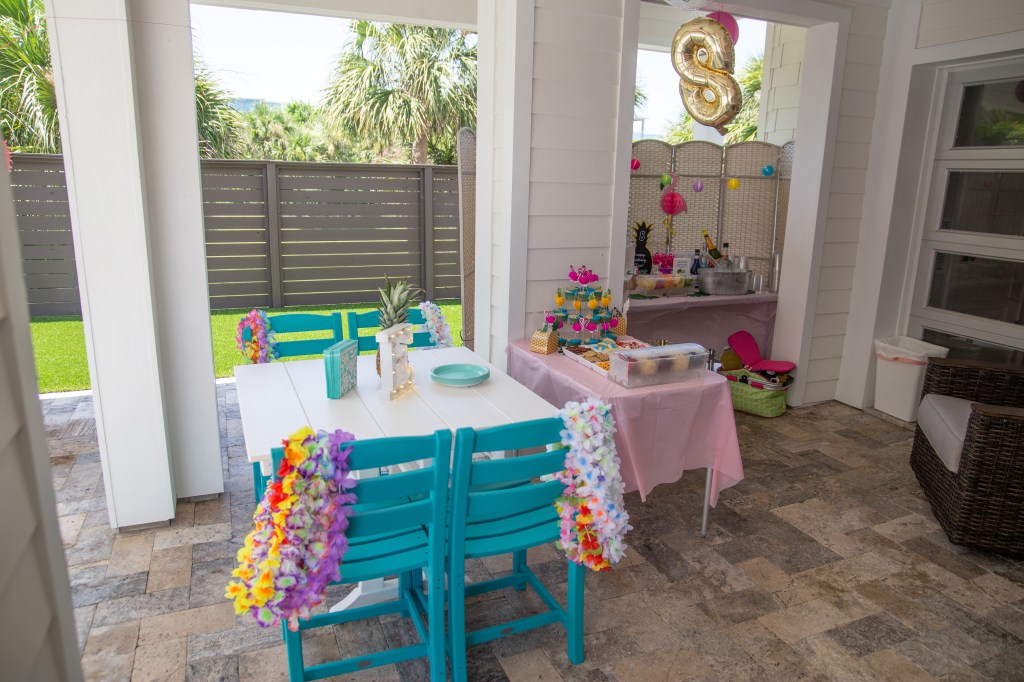 Overview of the decorated patio with lei-adorned turquoise chairs, snack table, and tropical drink station