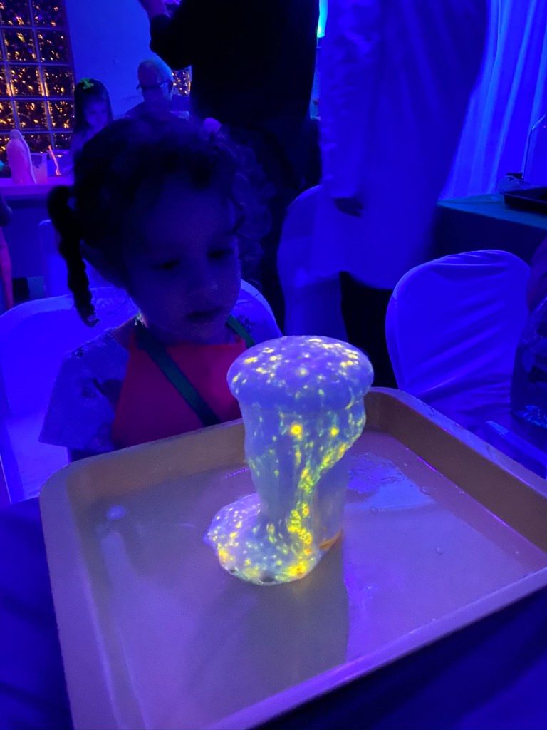 Tall column of glowing yellow-green foam under blacklight, with a child watching in awe.