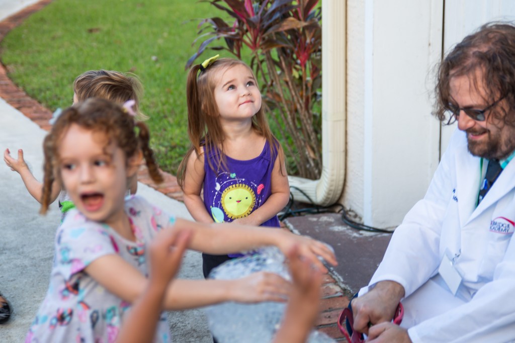 Young girl in purple dress gazing up at a floating helium bubble during an outdoor party.