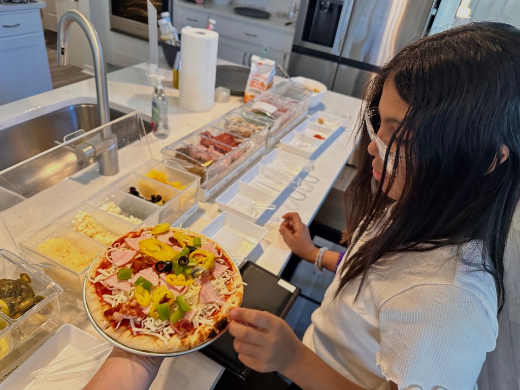 Child at pizza party building a personal pizza with toppings at the pizza station.