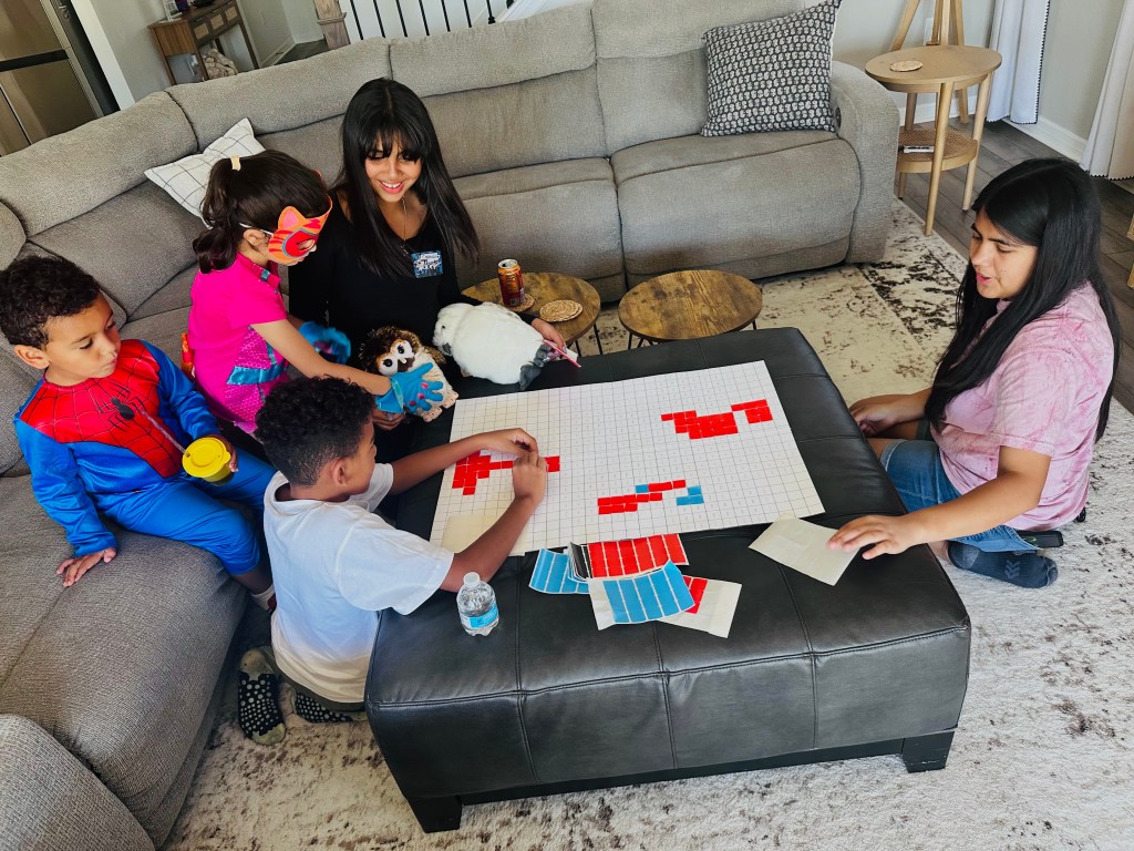 Children placing red stickers on a Spider-Man mystery mosaic grid at a birthday party.