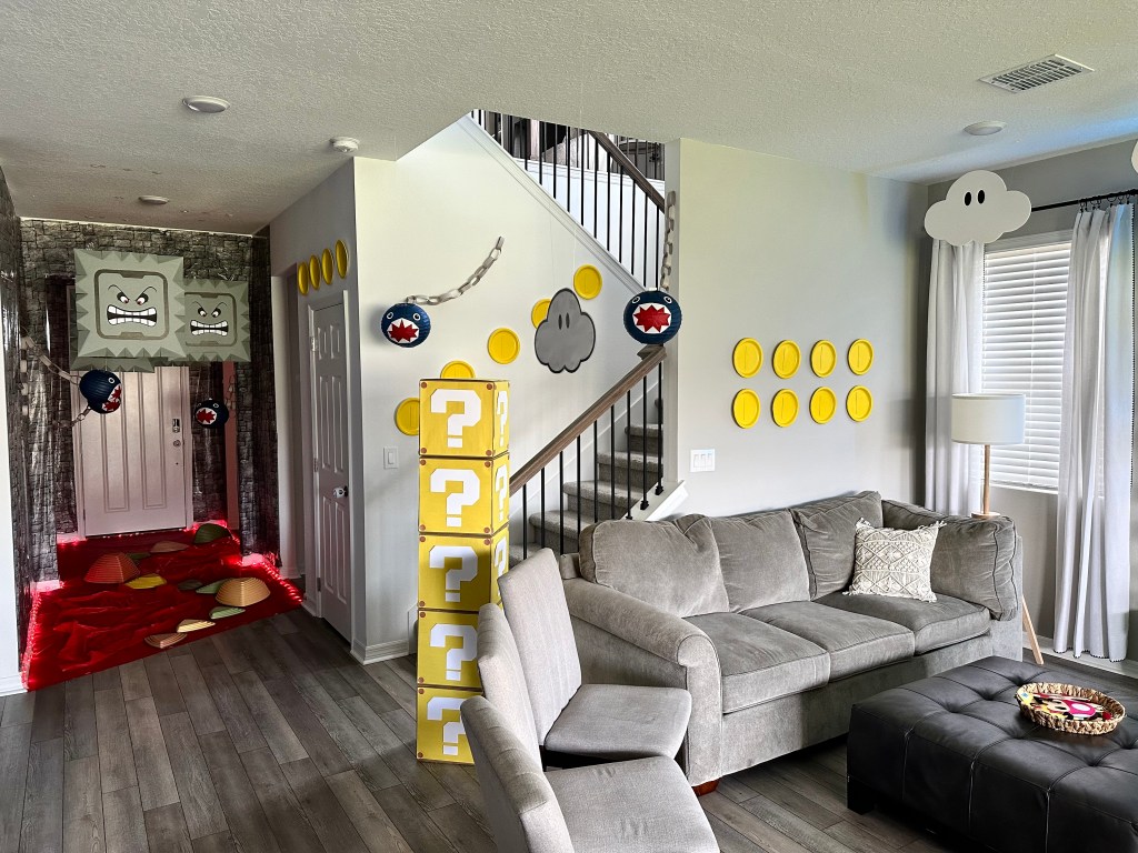 View of the Sky Land setup with balloon vines, floating clouds, and gold coin decorations on the walls. A few Chain Chomps can be seen hanging by the staircase, with the darker stone-themed entrance to Dark Land visible in the background.