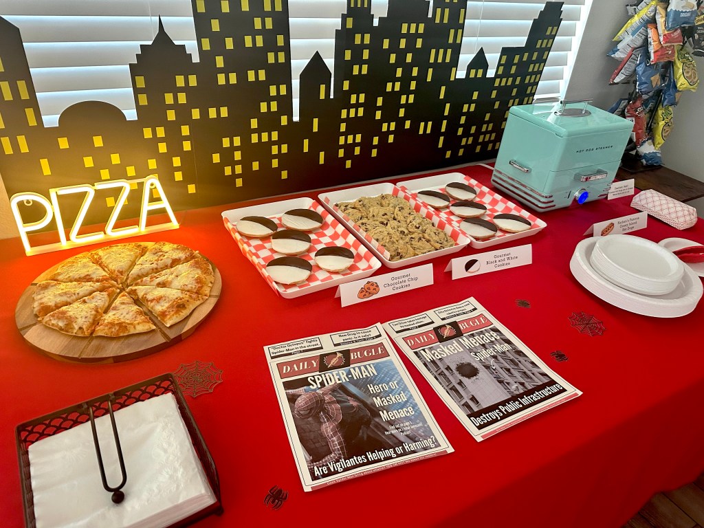 New York City party table with skyline backdrop, neon pizza sign, hot dog steamer, cookies, and fresh pizza.