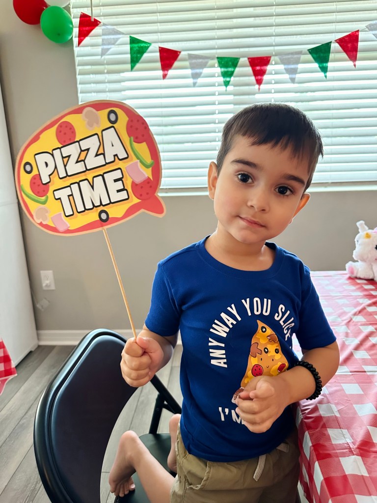 A boy posing with a playful pizza party props while waiting for his dinner.