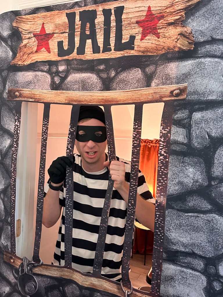Robber costume character behind a jail door party prop during a Spider-Man themed game.