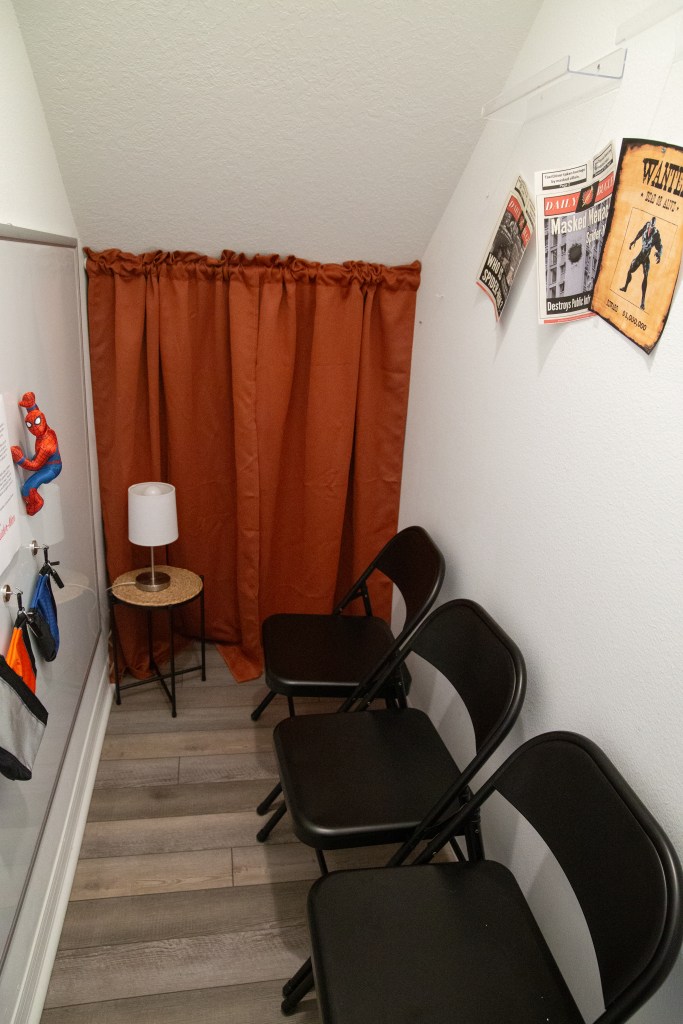 Inside view of the jail setup, with folding chairs lined against the wall, red curtain doorway, and themed villain posters on the wall.