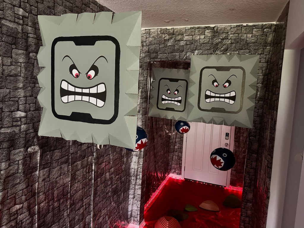 Super Mario party Dark Land hallway decorated with large hanging Thwomp blocks, Chain Chomp props, stone-patterned walls, red lava floor, and stepping stones.