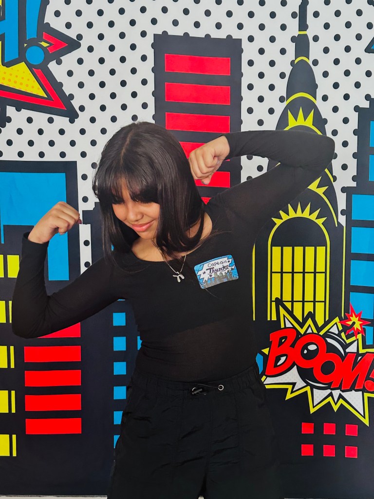 Party guest posing at a superhero backdrop wearing a name tag that says Captain Thunder, flexing muscles in character.