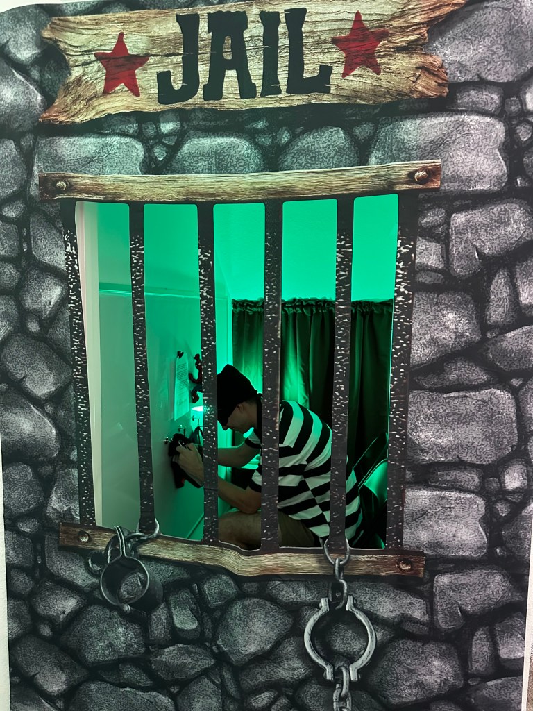A robber sits inside the party jail prop, trying to unlock a parole certificate bag with a combination lock during the Superheroes vs. Robbers game.