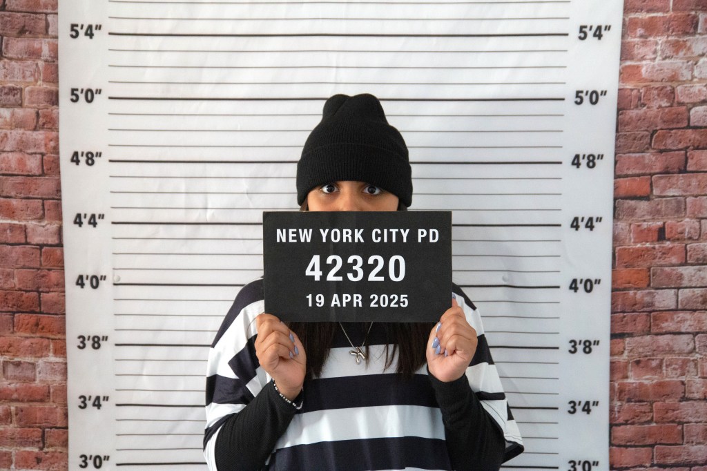 Child dressed as a robber holding a mugshot sign in front of a height chart backdrop during the Superheroes vs. Robbers party game.