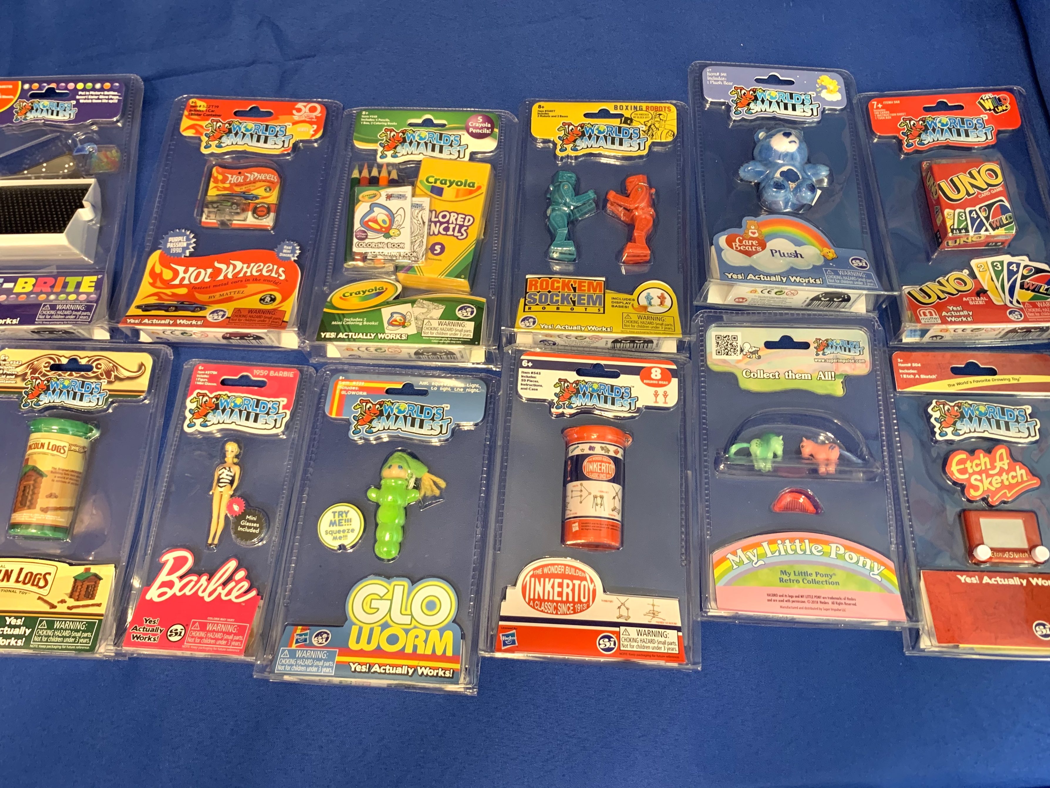 A collection of miniature packaged toys such as Lite-Brite, Barbie, Hot Wheels, Glo Worm, and Etch A Sketch displayed on a blue background as party favors.
