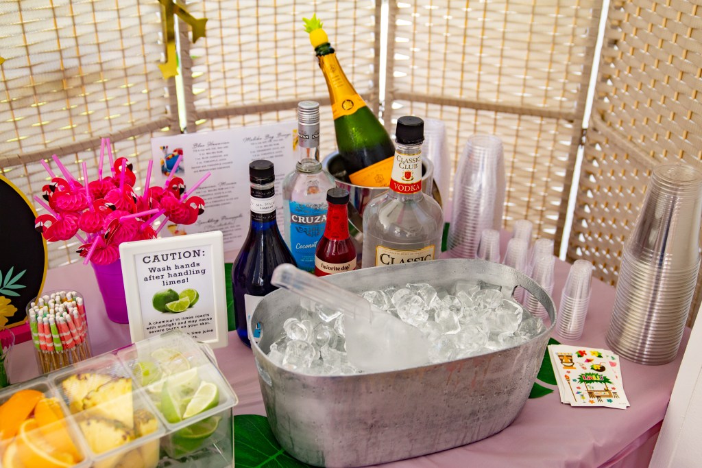 Ice-filled bucket with bottles of vodka, coconut rum, blue curaçao, and other mixers at a tropical party drink station.