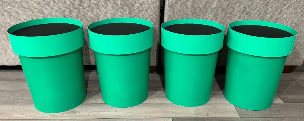 DIY Mario party warp pipes made from painted 5-gallon buckets with green poster board rims and black foam core tops, perfect for party decor or a bean bag toss game.