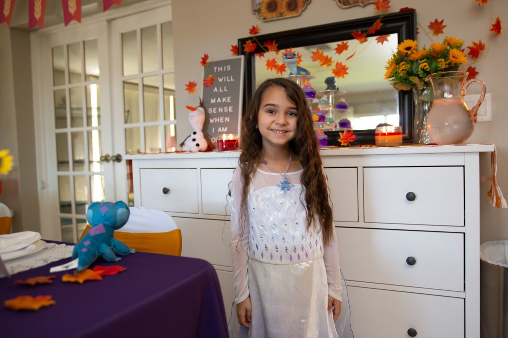 Birthday girl smiles in front of fall-themed decorations, cupcakes, and a sign that reads, “This will all make sense when I am older.”