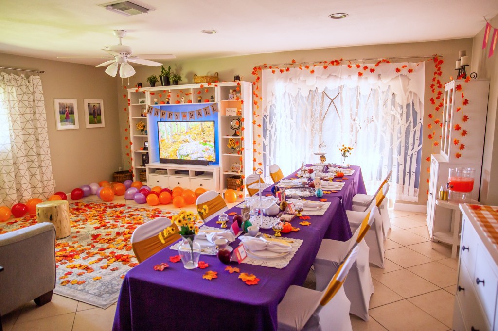 Full view of Frozen 2 fall-themed party setup in a living room with purple tablecloths, balloons, and leaf garlands