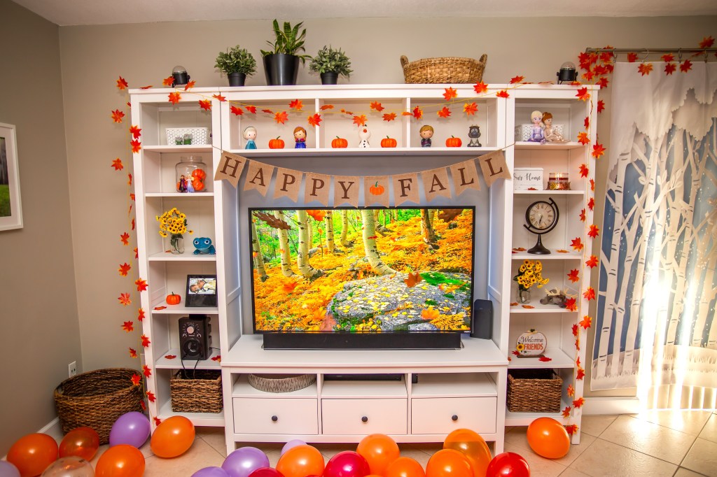 Entertainment center with fall leaf garland, Frozen 2 figurines, and “Happy Fall” banner across the TV