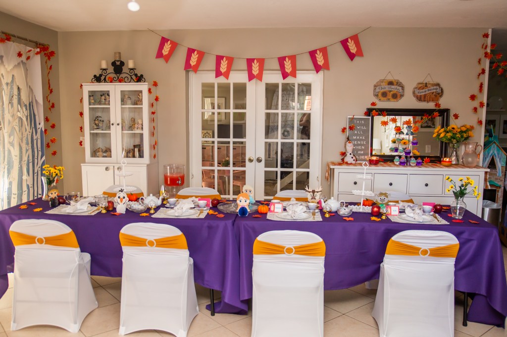 Tea party table with Frozen 2 themed decor and a handmade Arendelle banner in burgundy and pink hanging above