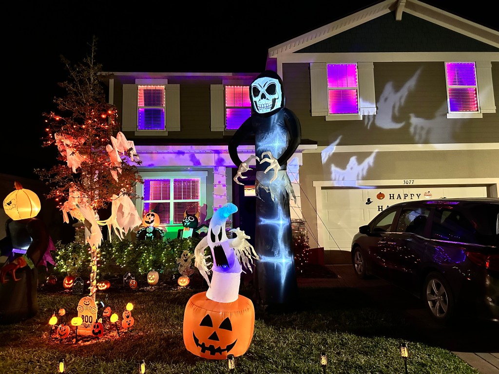 Front view of a house decorated for Halloween with purple lights, ghost inflatables, and a large grim reaper inflatable for a Ghostbusters-themed setup.