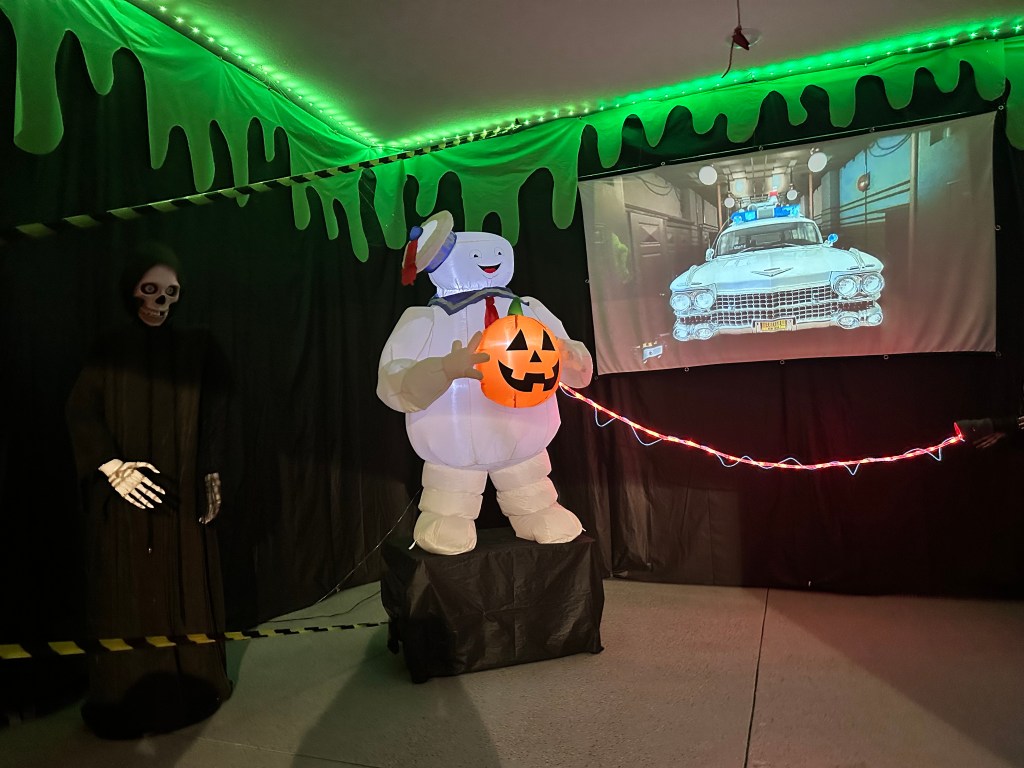 Ghostbusters Halloween garage setup featuring Stay Puft, a jack-o’-lantern, a projection of the Ecto-1, and a skeleton reaper.