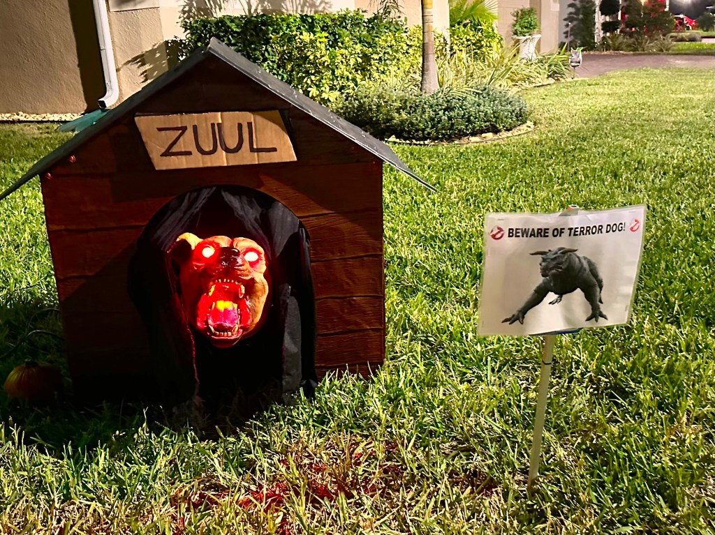 DIY Ghostbusters display featuring a realistic Zuul Terror Dog prop in a red doghouse with glowing red eyes and a warning sign.