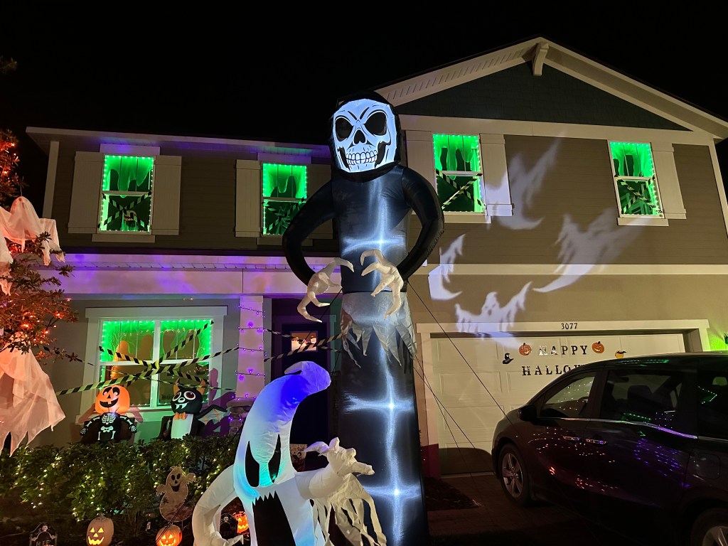 Halloween house lit up with green lights and caution tape, showing Ghostbusters-style slime effects and silhouette ghosts in the windows.