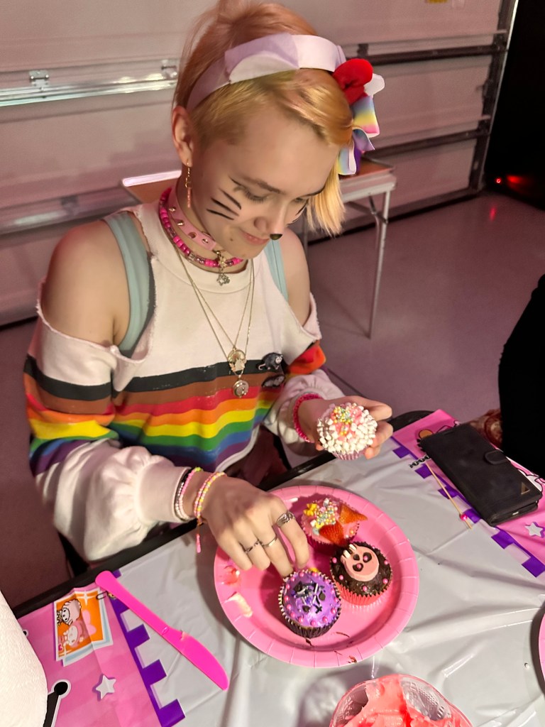 Teen guest placing toppings on decorated cupcakes at a party table.