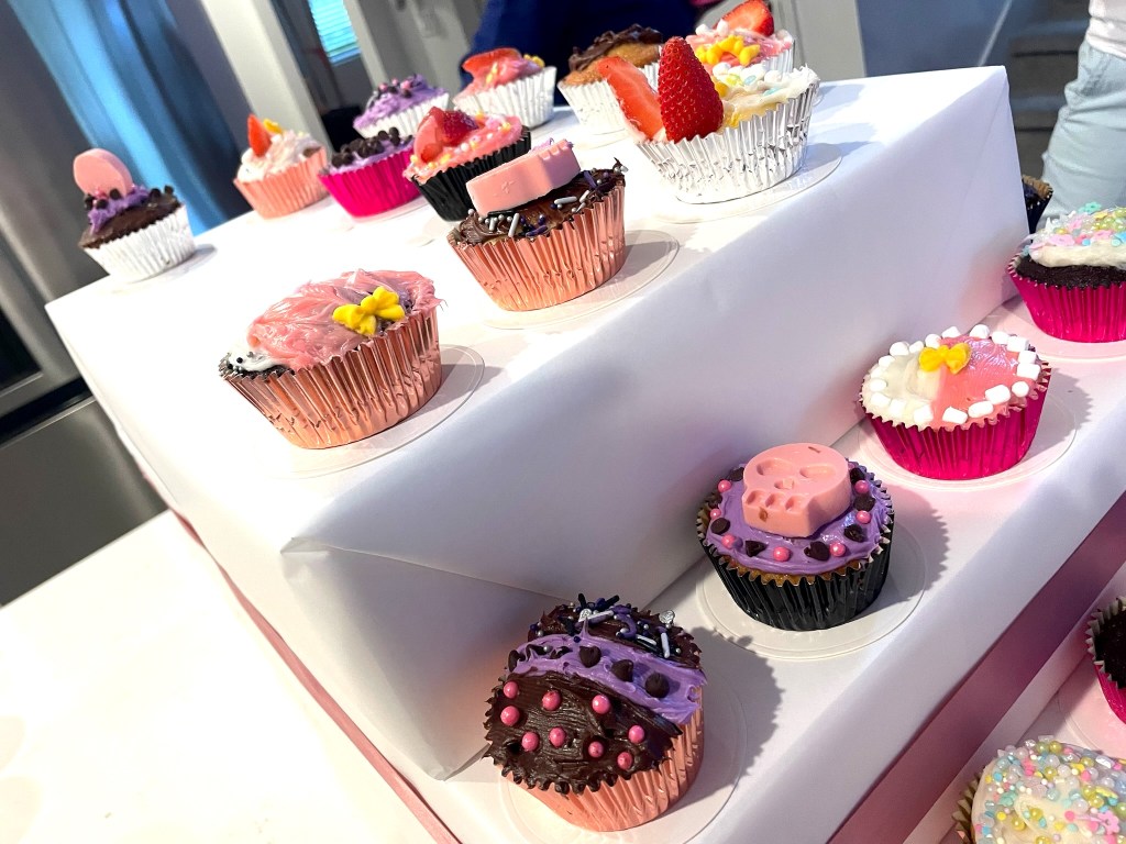 Close-up view of decorated cupcakes featuring pink chocolate skulls, strawberries, and colorful sprinkles, displayed on a white tiered stand.