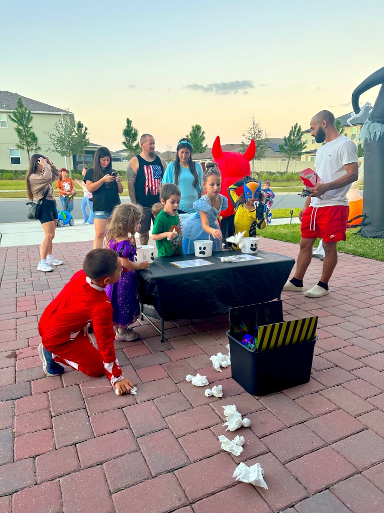 Children in Halloween costumes playing the Ghostbusters toss game by aiming DIY tissue ghosts into a glowing trap bucket.