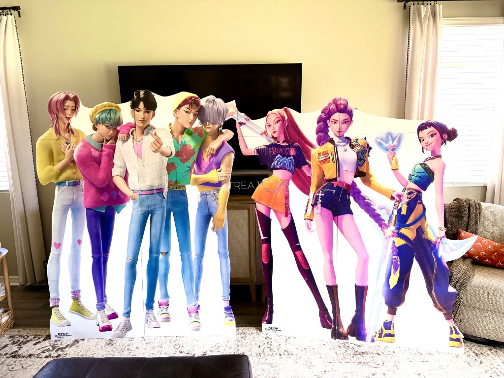 Life-size cardboard standees of the K-Pop Demon Hunters characters arranged inside a living room.