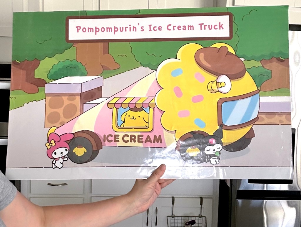 A finished giant party sign being held up, featuring a colorful Pompompurin ice cream truck design.