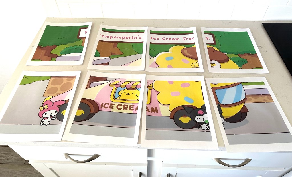 Multiple sheets of paper laid out on a counter, each showing a section of a large Sanrio ice cream truck image, ready to be assembled into a poster.
