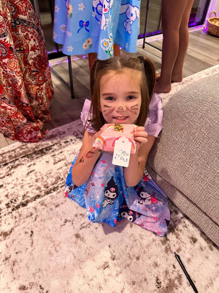 Smiling girl in face paint and Kuromi dress holding a wrapped bracelet gift.
