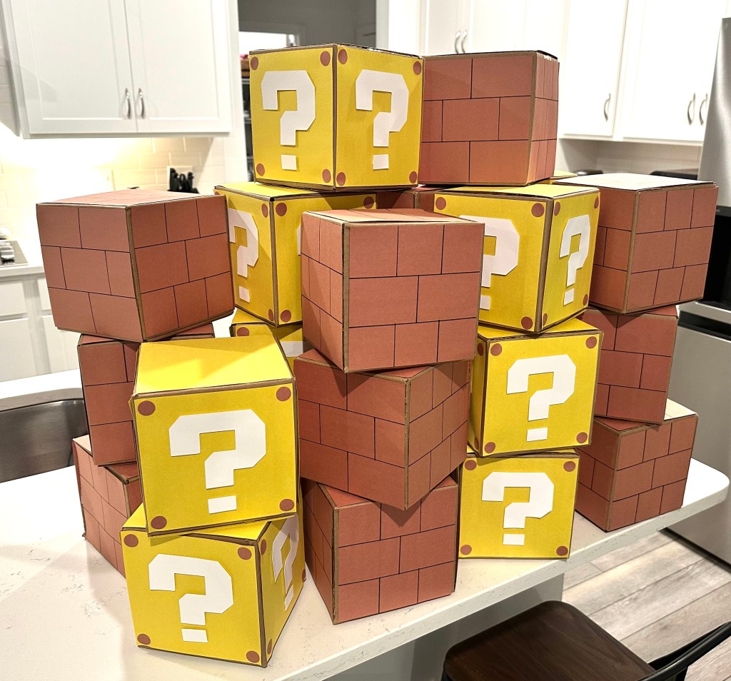 A stack of DIY Mario-themed Brick and Question Blocks made from cardboard boxes, decorated with  designs to resemble blocks from the Super Mario video games.