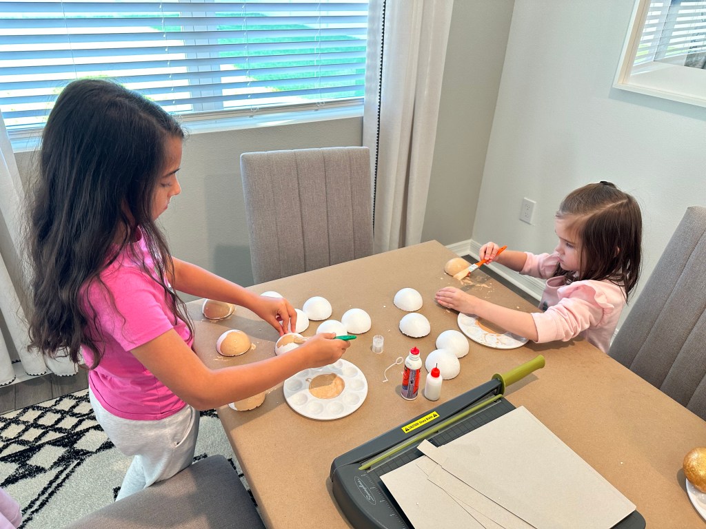 Two children painting styrofoam halves to create Goomba feet bases for a DIY Mario party decoration project.