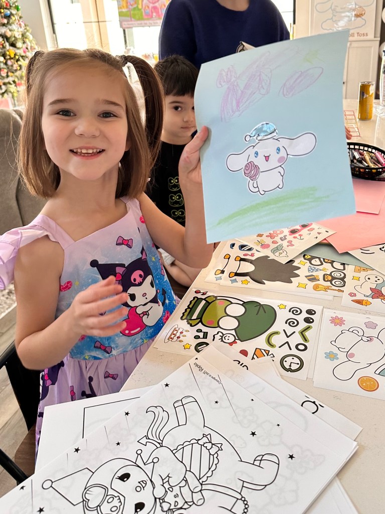 Young girl sitting at a table with crayons and Sanrio coloring pages, keeping busy before the Hello Kitty-themed birthday party begins.