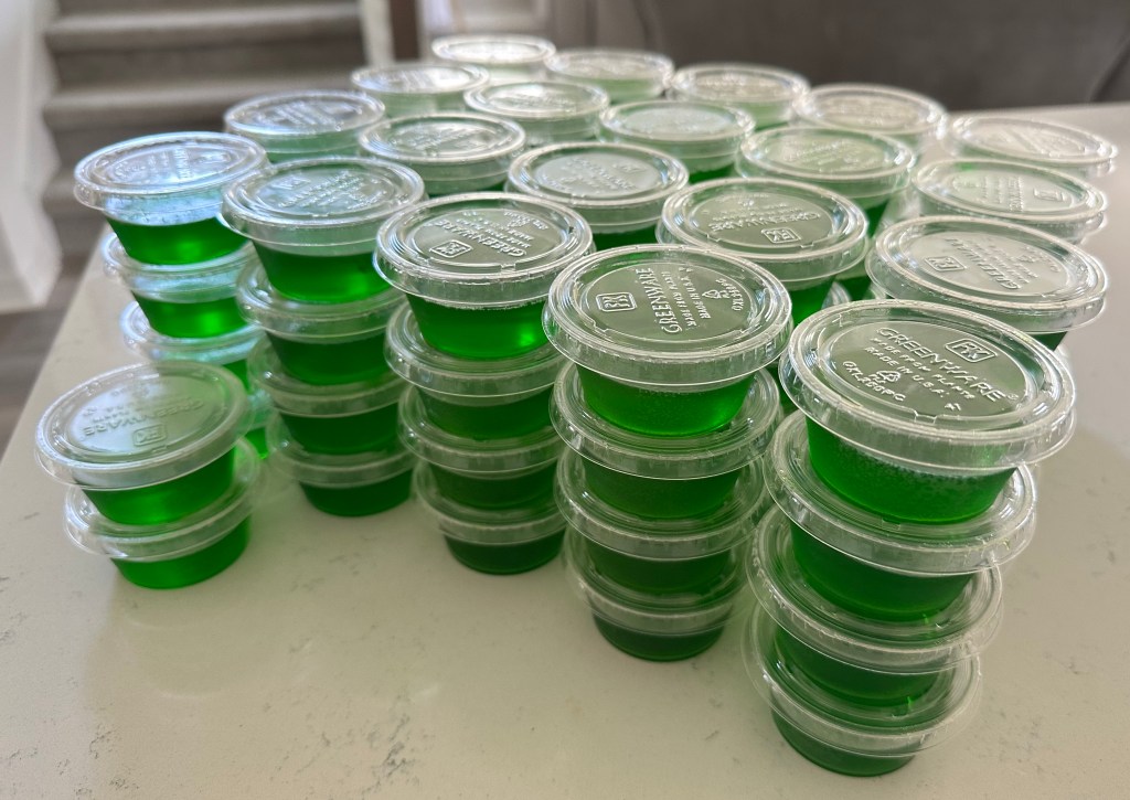 Stacks of green jello shots in plastic cups on a counter, made with apple cinnamon flavor and Fireball whiskey, themed after Slimer from Ghostbusters.